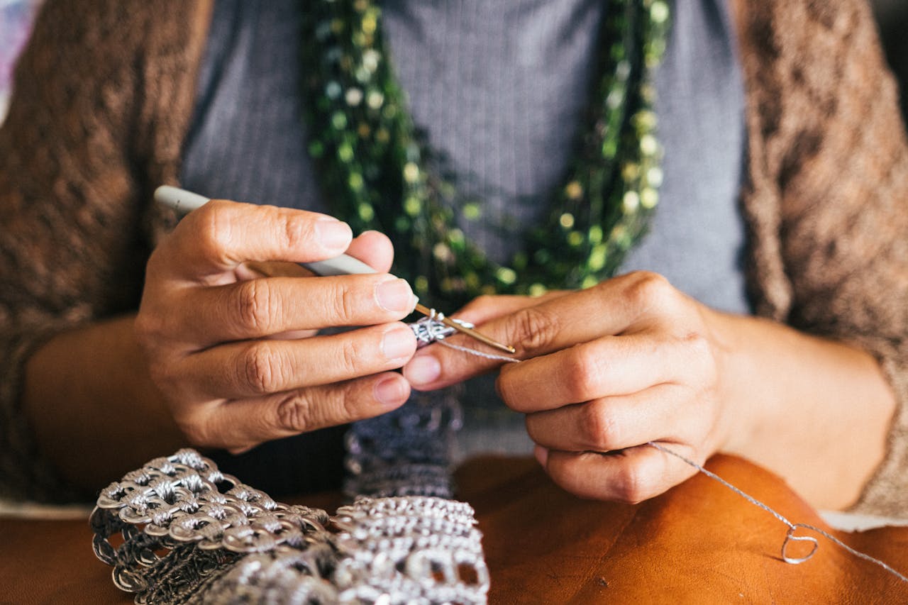 Close-up of a woman creating jewelry using crochet techniques with metal yarn, showcasing skill and creativity.