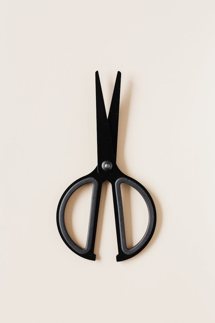 Top view of simple black scissors placed vertical on beige surface