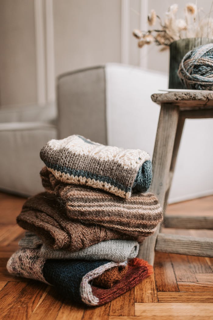 A stack of folded knitted scarves in earthy tones sitting on a rustic wooden chair indoors.