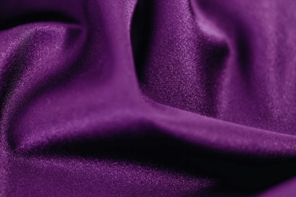 Detailed close-up image of rich purple fabric with smooth texture and elegant folds, ideal for textile and fashion backgrounds.
